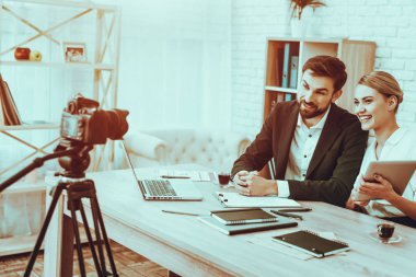 Blogcular bir Video yapar. Blogcular gülümseyen genç erkek ve kadın var. Video ile ilgili bir iş. Kamera bir Video vuruyor. Becerikli alet ve malzemeleri masada. Bir kameraya bakan kişiler. Studio iç insanlarda.