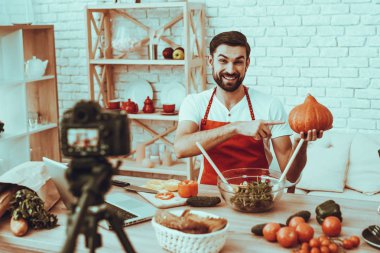 Blogger bir Video yapar. Blogger gülümseyen sakallı adam Video hakkında bir yemek olduğunu. Kamera bir Video vuruyor. Laptop ve farklı yemek masada. Balkabağına gösterilen adam. Studio iç adam.