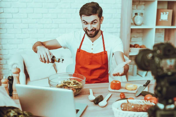 Blogger Makes a Video. Blogger is Smiling Beard Man. Video About a Cooking. Camera Shoots a Video. Laptop and Different Food on Table. Man is Pouring Oil in Salad. Man in Studio Interior.