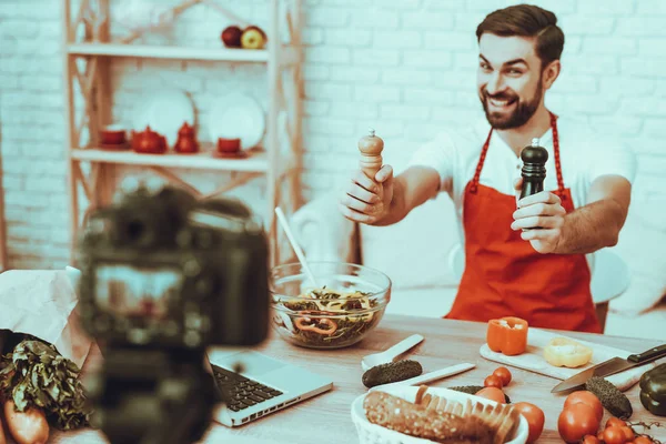 Blogger Makes a Video. Blogger is Smiling Beard Man. Video About a Cooking. Camera Shoots a Video. Laptop and Different Food on Table. Man Showing a Seasonings. Man in Studio Interior.