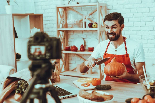 Blogger Makes a Video. Blogger is Smiling Beard Man. Video About a Cooking. Camera Shoots a Video. Laptop and Different Food on Table. Man Showing He Want Cuts a Pumpkin. Man in Studio Interior.
