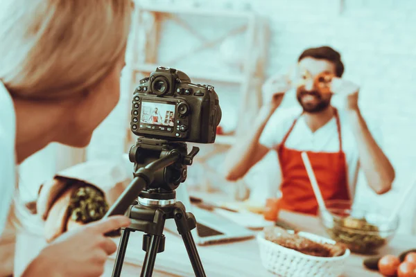 Blogger Makes a Video. Blur View of Blogger. Video About a Cooking. Woman Operator Shoots a Video on Camera. Different Food on Table. Man Showing a Pieces of Pepper. People in Studio Interior.