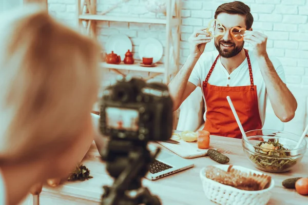 Blogger Makes a Video. Blogger is Smiling Beard Man. Video About a Cooking. Woman Operator Shoots a Video on Camera. Different Food on Table. Man Showing a Pieces of Pepper. People in Studio Interior.