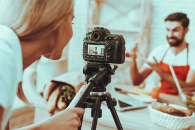 Blogger bir Video yapar. Blogger görünümünü bulanıklık. Bir pişirme hakkında video. Kadın işleç bir Video kameraya ateş eder. Farklı yemek masada. Biber bir parçası gösterilen adam. Studio iç insanlarda.