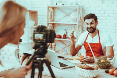 Blogger bir Video yapar. Blogger gülümseyen sakallı adam Video hakkında bir yemek olduğunu. Kadın işleç bir Video kameraya ateş eder. Farklı yemek masada. Biber bir parçası gösterilen adam. Studio iç insanlarda.