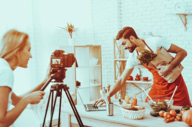 Mutlu bir adam Blogger bir Video yapar. Bir pişirme hakkında video. Kadın işleç bir Video kameraya ateş eder. Farklı yemek masada. Bir ürün tutan ve bir dizüstü bilgisayar kullanarak bir adam. Studio iç insanlarda.