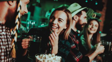 Adam komik şapkalı bir kız ile patlamış mısır yiyor. Bira aperatifler. Alkol kullanımı. Kızıl Sakal. Gülümseyen. İyi şenlikli ruh hali. Parlak ışıklar. Club ziyaretçi. Komik şapkalar. Bardakları tokuşturup.