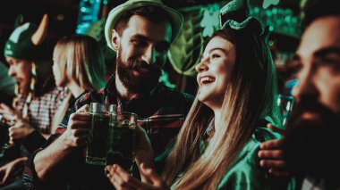 Genç şirket St Patrick's Day kutluyor. Bar Counter. Alkol kullanımı. Siyah sakallı. Gülümseyen. Karnaval giysileri. Parlak ışıklar. Club ziyaretçi. Komik şapkalar. Bira içme.