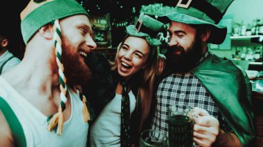 İki erkek ve kız Carnival şapka bira içiyor. St Patrick's Day kavramı kutlama. Bar Counter. Sakallı erkekler. İyi şenlikli ruh hali. Parlak ışıklar. Club ziyaretçi. Eğleniyor. Birlikte dinlenme.