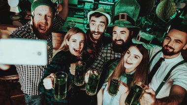 Selfie barda genç şirket var. St Patrick's Day. Bar Counter. Alkol kullanımı. Siyah sakallı. Gülümseyen. İyi şenlikli ruh hali. Parlak ışıklar. Club ziyaretçi. Komik şapkalar. Bira ile gözlük.