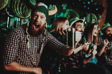 Komik şapkalı adam St Patrick's Day kutluyor. Bar Counter. Alkol kullanımı. Kızıl Sakal. Gülümseyen erkek. İyi şenlikli ruh hali. Parlak ışıklar. Eğlence kulübü ziyaretçi. Ağzını aç. Bardak bira.