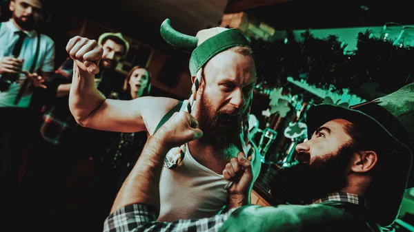 Two Men Fight In Pub. Saint Patrick\'s Day Concept. Punch In The Face. Quarrel In The Bar. White Singlet. Agressive Males. Angry Guys. Violence In The Club. Funny Hats. Bright Lights.