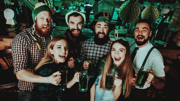 Young Company Are Celebrating St Patrick\'s Day. Bar Counter. Alcohol Handling. Black Beard. Smiling Teenagers. Good Festive Mood. Bright Lights. Club Visitors. Funny Hats. Glasses With Beer.