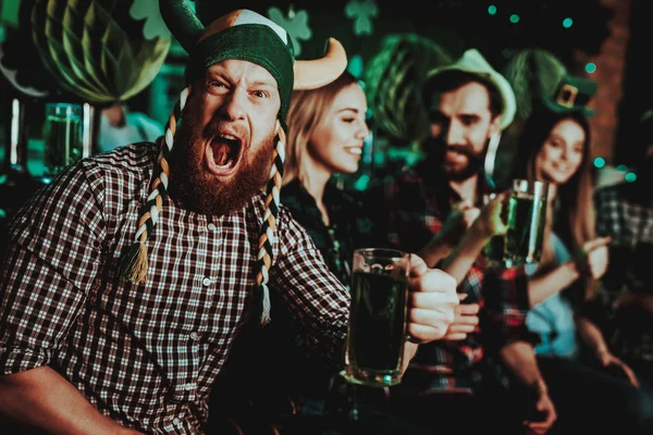 戴着滑稽帽子的人庆祝圣帕特里克节 酒吧柜台 酒精处理 姜胡子 微笑的男性 良好的节日心情 明亮的灯光 有趣的俱乐部访客 张开嘴 一杯啤酒 — 图库照片
