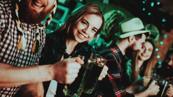 Man In Funny Hat Is Drinking Beer With A Girl. Bar Counter. Alcohol Handling. Ginger Beard. Smiling Teenagers. St Patrick\'s Day Celebrating. Bright Lights. Club Visitors. Glasses Clinking.