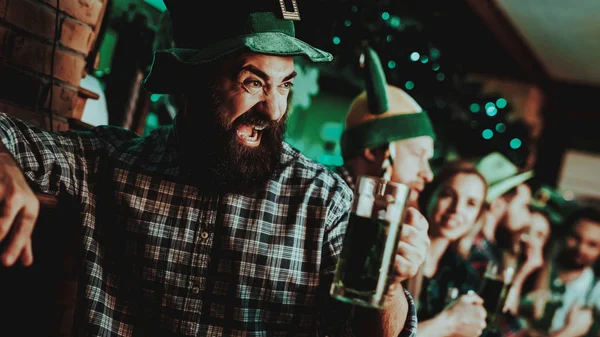 Guy In The Leprechaun Cap Is Drinking A Beer. Bar Counter. Alcohol Handling. Black Beard. Smiling Male. Good Festive Mood. Bright Lights. Funny Club Visitor. Open Mouth. St Patrick\'s Day.