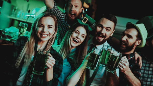 Young Company Are Celebrating St Patrick\'s Day. Bar Counter. Alcohol Handling. Black Beard. Smiling Teenagers. Good Festive Mood. Bright Lights. Club Visitors. Funny Hats. Glasses With Beer.