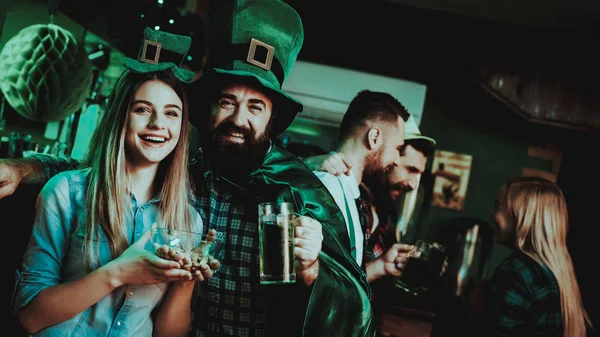 Man In Funny Hat Is Drinking Beer With A Girl. Bar Counter. Alcohol Handling. Ginger Beard. Smiling Teenagers. St Patrick\'s Day Celebrating. Bright Lights. Club Visitors. Plate With Pistachios.