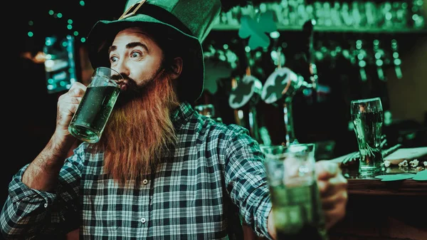 Guy In The Leprechaun Cap Is Drinking A Beer. Bar Counter. Alcohol Handling. Black Beard. Smiling Male. Good Festive Mood. Bright Lights. Funny Club Visitor. Open Mouth. St Patrick\'s Day.