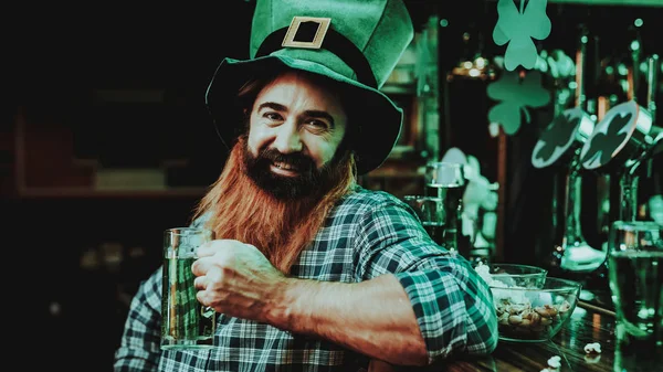 Guy In The Leprechaun Cap Is Drinking A Beer. Bar Counter. Alcohol Handling. Black Beard. Smiling Male. Good Festive Mood. Bright Lights. Funny Club Visitor. Open Mouth. St Patrick\'s Day.