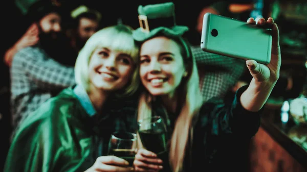 Two Girls Do Selfie In Pub. St Patrick\'s Day Celebrating Concept. Bar Counter. Good Festive Mood. Bright Lights. Club Visitors. Having Fun. Resting Together. Memory Photo. Smiling Women.