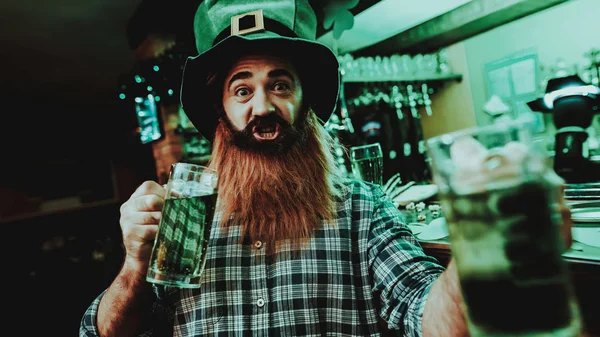 Guy In The Leprechaun Cap Is Drinking A Beer. Bar Counter. Alcohol Handling. Black Beard. Smiling Male. Good Festive Mood. Bright Lights. Funny Club Visitor. Open Mouth. St Patrick\'s Day.