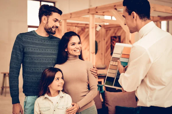 Young Family Consulting With Furniture Seller. Happy Together. Bright Office. Sunny Day.Manager In Shirt And Tie. Business Meeting. Room Interior. Parents And Daughter. Look Around The Store.