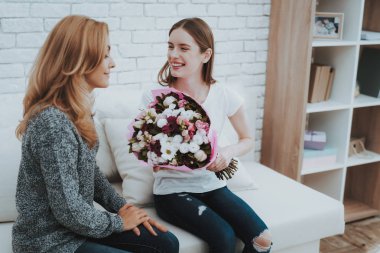 Gülümseyen kızı anne çiçek ve hediye verir. Aile ilişkisi var. Tatil evde. Mutlu anne. Dostluk ilişkileri. Birlikte kutluyor. Aile kavramı mutluluk. Hediye sunma.