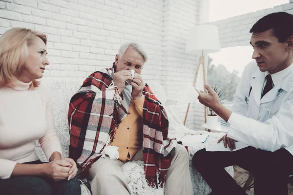 Young Doctor in Coat Visiting Old Couple at Home. Medical Healthcare Concept. Man in White Coat. Sitting on Sofa. Old Man with Blanket. Grandfather and Grandmother. People with Gray Hair.