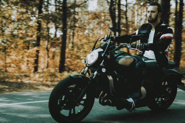 Bir ormandaki karayolu üzerinde motosiklet motosiklet sürmek... Araç hız. Serin binici ile bir deri ceket. Motosiklet kavramı. Klasik tarzı. Sürücü için hazır. Bir ormandaki hız motosiklet. Hızlı sürücü.