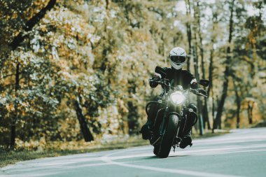 Motosiklet kask içinde bir ormandaki karayolu üzerinde biniyor. Araç hız. Serin binici ile bir deri ceket. Motosiklet kavramı. Klasik tarzı. Sürücü için hazır. Bir ormandaki hız motosiklet. Gizli yüz.