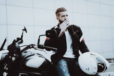 Deri ceketli adamı motosiklet üzerinde sigara içiyor. Geziye gidiyor. Moda binici. Kendine güvenen bakışları. Araç hız. Havalı motorcu sakallı. Motosiklet kavramı. Klasik tarzı. Sürücü hazır.