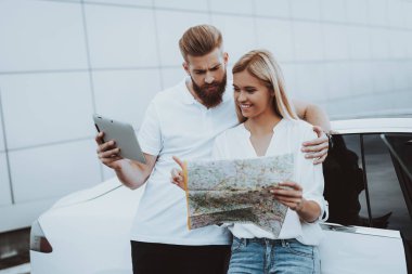 Çift Tesla araba ile ayakta harita üzerinde arıyor. Şarj istasyonu. Otomobil arka plan. Yenilik teknoloji. Yeni nesil Electro hibrid araç. Güneşli bir gün. Futuristik güç. Otopark.