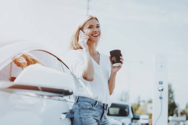 Tesla araba şarj kavramı. Kız telefonda konuşuyor. Otomobil istasyonu. Yenilik teknoloji. Yeni nesil Electro hibrid araç eklenti. Ekoloji istasyonu. Futuristik güç. Kahve.