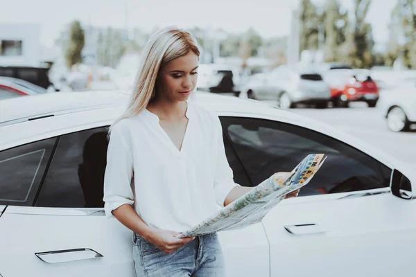 女の子はテスラ車の横に立っている地図を探しています 充電ステーション 自動車の背景 旅の計画 新世代電気ハイブリッド車 晴れた日 方法を見つけます 駐車場 — ストック写真