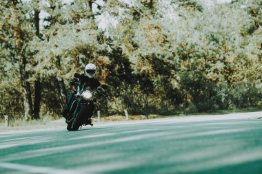 Motosiklet kask içinde bir ormandaki karayolu üzerinde biniyor. Araç hız. Serin binici ile bir deri ceket. Motosiklet kavramı. Klasik tarzı. Sürücü için hazır. Bir ormandaki hız motosiklet. Gizli yüz.