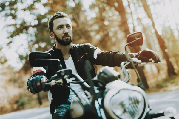 Motorcycle Biker Rides On Highway In A Forest.. Speed Vehicle. Cool Rider With A Leather Jacket. Motorbike Concept. Classic Style. Ready To Drive. Speed Motorcycle In A Forest. Quick Driver.