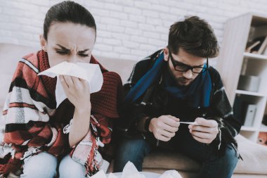 Evde kanepe üzerinde battaniye ile hasta genç çift. Erkek ve kadın kanepe. Damalı battaniye. Ev Concept, sağlık. Oda beyaz kanepe. Evde hasta adam sağlık. Ahşap masa.