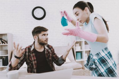 Young Upset Woman Cleaning Room with Lazy Man. Sanitary at Home. Hands in Rubber Gloves. Housekeeping Concept. Cleaning with Sponge. Using Spray. Family at Home. Couple Indoor. Sanitary Concept. clipart