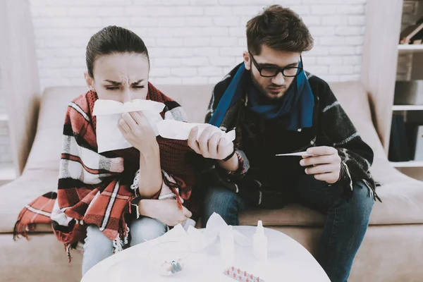 Sick Young Couple with Blankets on Sofa at Home. Man and Woman on Sofa. Checkered Blanket. Healthcare at Home Concept. White Sofa in Room. Sick Man. Healthcare at Home. Wooden Table.