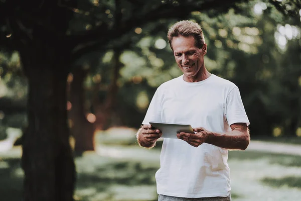 Hombre de pie en el parque de verano y el uso de la tableta . — Foto de Stock