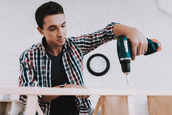 Young Man Assembling Wooden Bookshelf at Home. Wooden Bookcase. Selfmade Furniture. Man and Hobby. White Room. Engineer with Tool. Young Man at Home. Homemade Decoration. Modern Furniture.