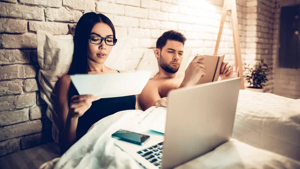 Молодая пара в постели, девушка работает ноутбук скучно человек — стоковое фото