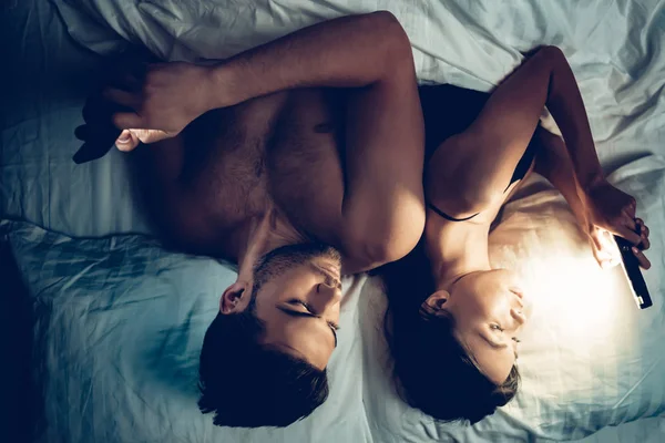 Casal apaixonado na cama usando telefone celular à noite — Fotografia de Stock