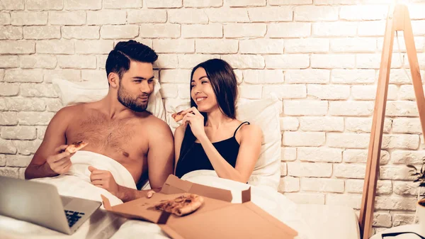 Casal amoroso assistindo filme comendo pizza na cama — Fotografia de Stock