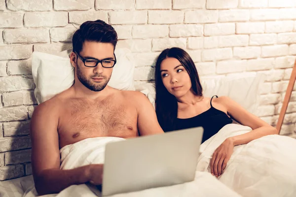 Молодая пара в постели, мужчина работает ноутбук скучно жены — стоковое фото
