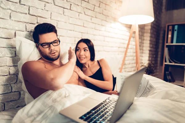 Pareja joven en la cama, Hombre Trabajando Esposa aburrida portátil —  Fotos de Stock