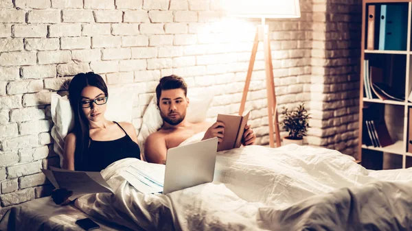 Молода пара в ліжку, дівчина робочий ноутбук знуджений чоловік — стокове фото