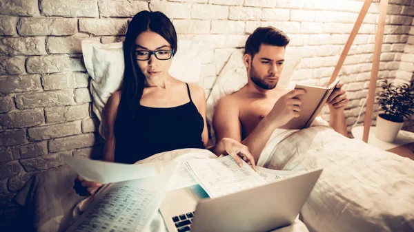 Para przy użyciu laptopa czytanie książki przed snem — Zdjęcie stockowe