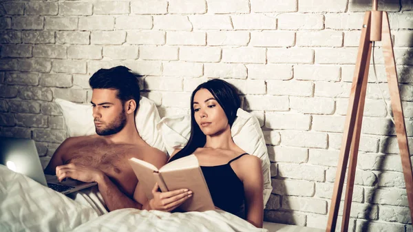 Casal usando laptop leitura livro antes de dormir — Fotografia de Stock